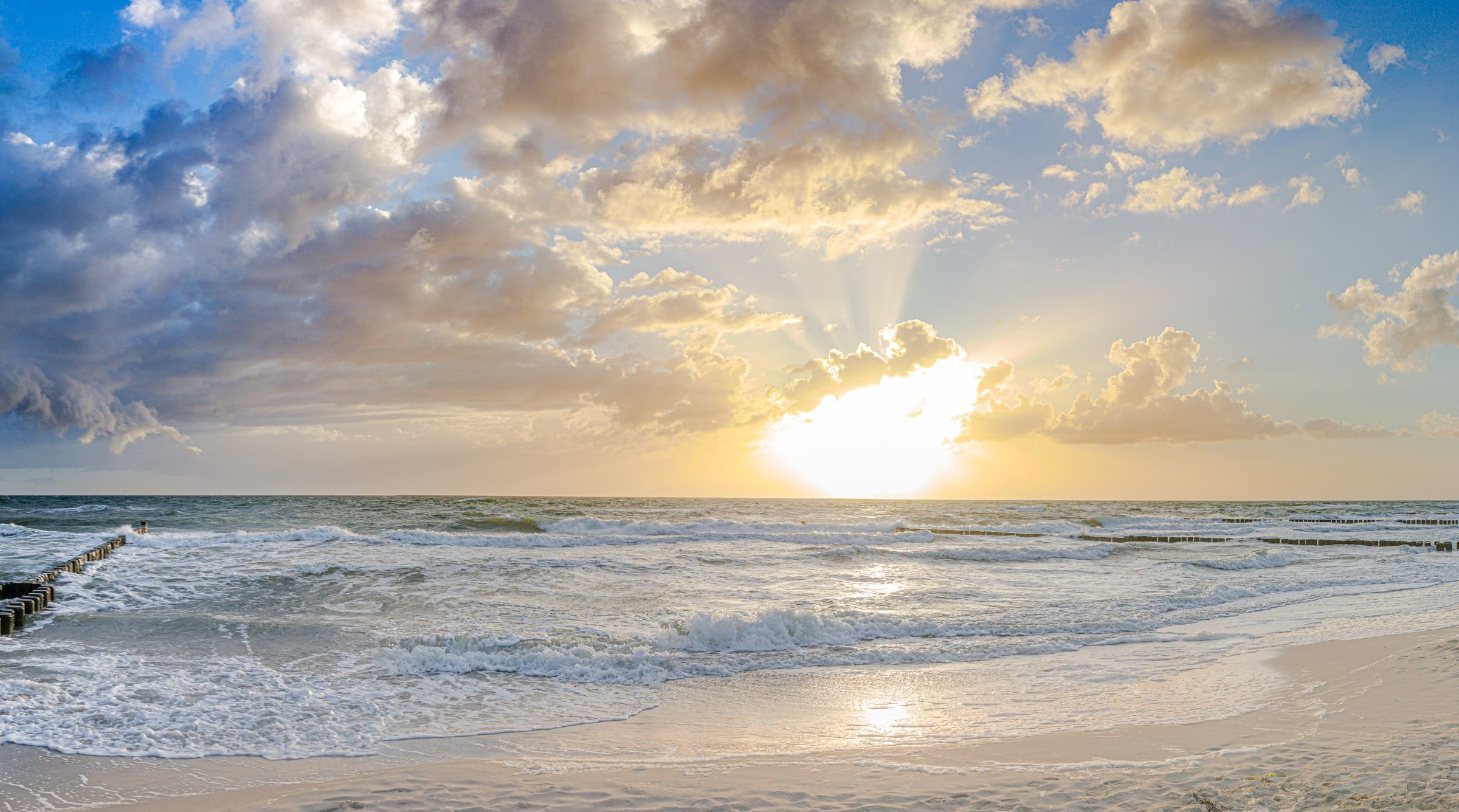 Sonnenuntergang über dem Meer, Wellen laufen auf einen Strand mit Buhnen